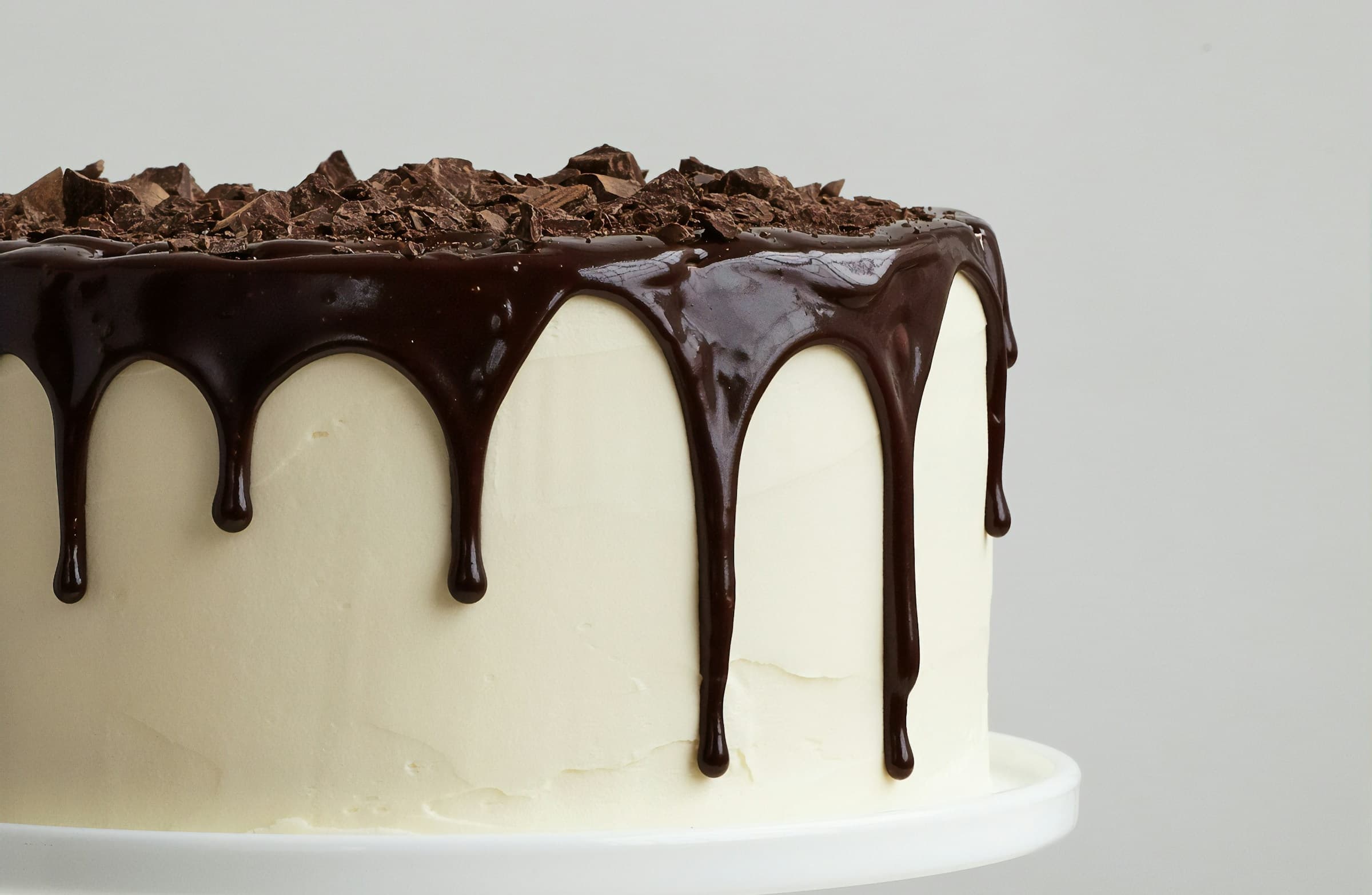 White frosted cake with glossy chocolate ganache drips and chocolate shavings